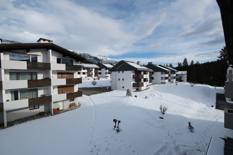 Modern white apartment buildings, balconies, large snow-covered area, parking lot