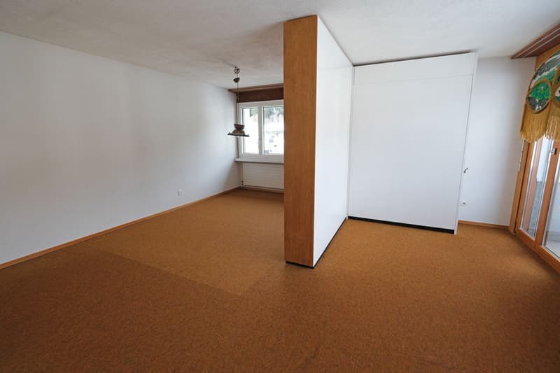 Empty room with white walls, wooden floors, central pillar, windows, sliding glass door