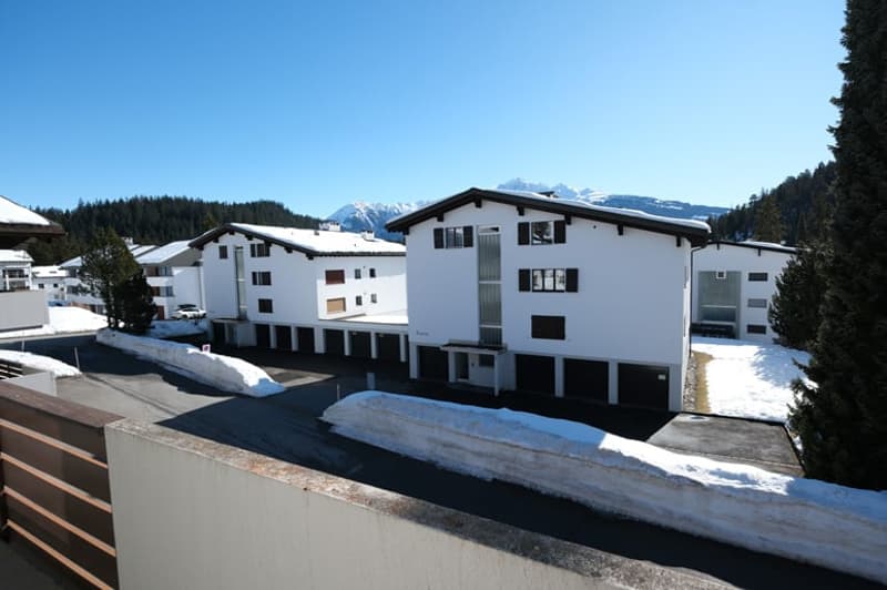 White building with multiple garages, snow on the ground, mountains in the background