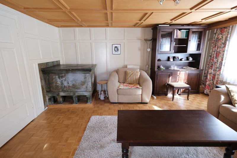 wooden floor, white walls, fireplace, wooden cabinet, armchair, coffee table, rug, stool