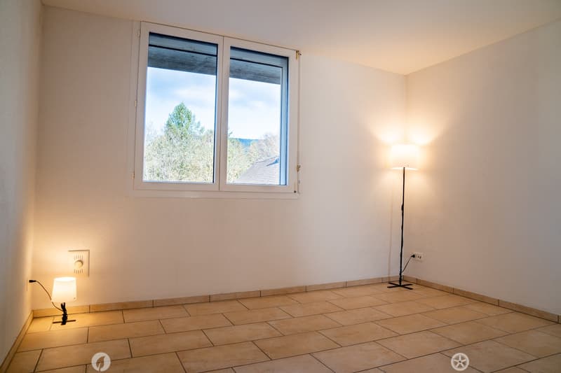 empty room with white walls, beige tiles, floor lamp, wall lamp, window with trees outside