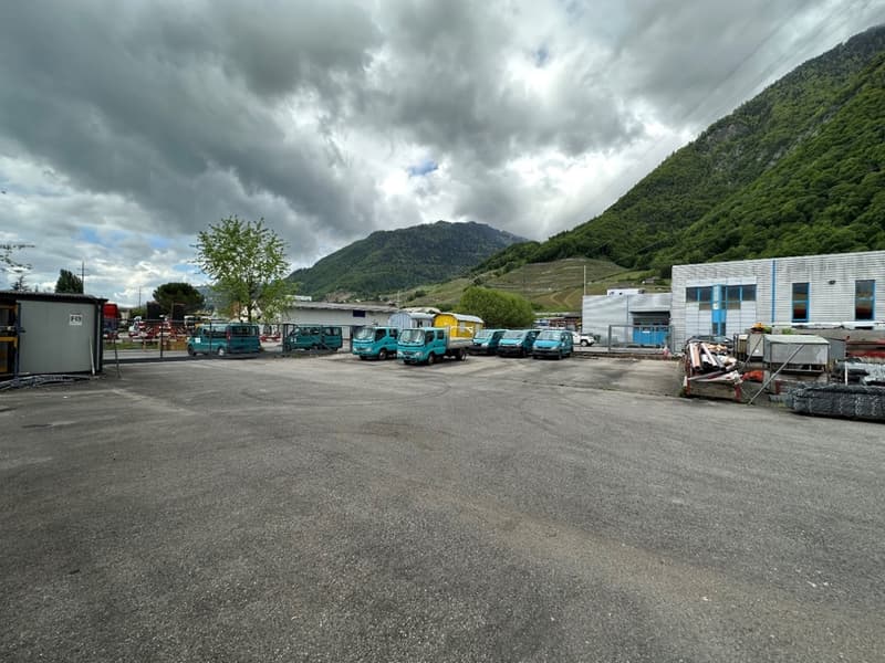 Outdoor parking lot with various commercial vehicles parked, surrounded by mountains and cloudy sky