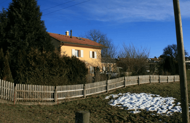 Two story house, red roof, yellow walls, white shutters, trees, snow