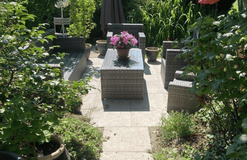 outdoor seating area with rattan couch, center table, flower pot, surrounded by green plants
