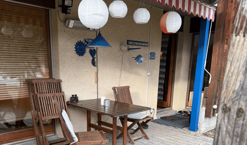 outdoor dining set, wooden chairs, hanging lanterns, table with cups and plates, slippers by the door, wall decorations