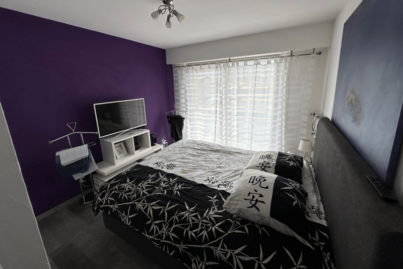 Bedroom with purple wall, bed, nightstands, TV, curtains, remote on headboard