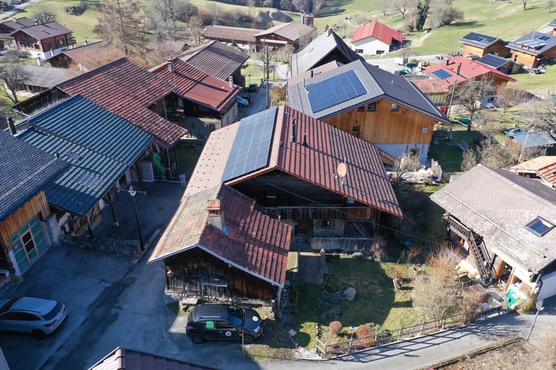 Wooden and brick houses with solar panels on the roofs, a parking lot with 2 cars parked, several chimneys, green lawn with small plants