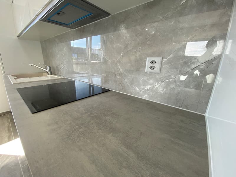 modern kitchen with gray marble countertop, black induction hob, white sink, gray marble backsplash, electrical outlet, stainless steel faucet