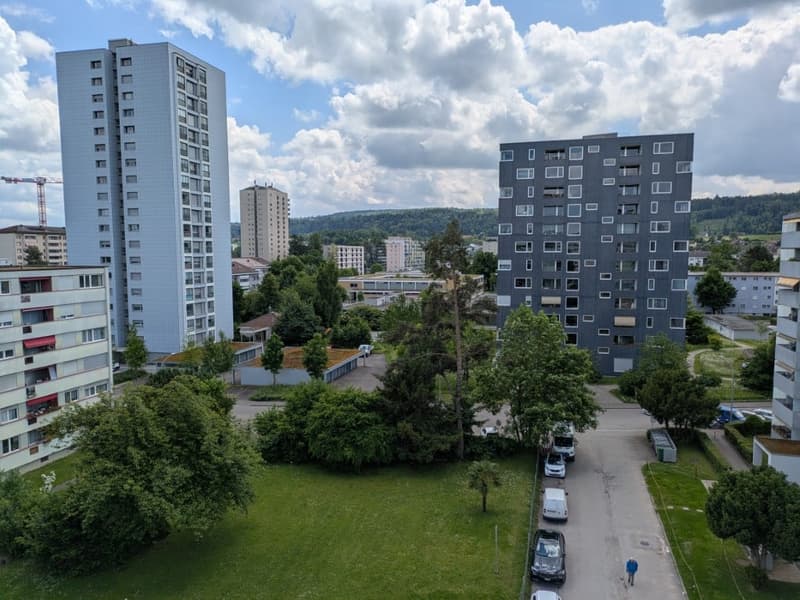 Three tall buildings, parking lot, road, person walking, cars parked