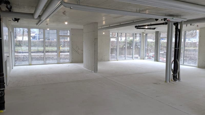 An empty room with white floor, large glass windows, white walls, visible ceiling and pipes