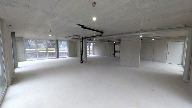 Empty room with concrete walls, large windows, metal beams and pipes.