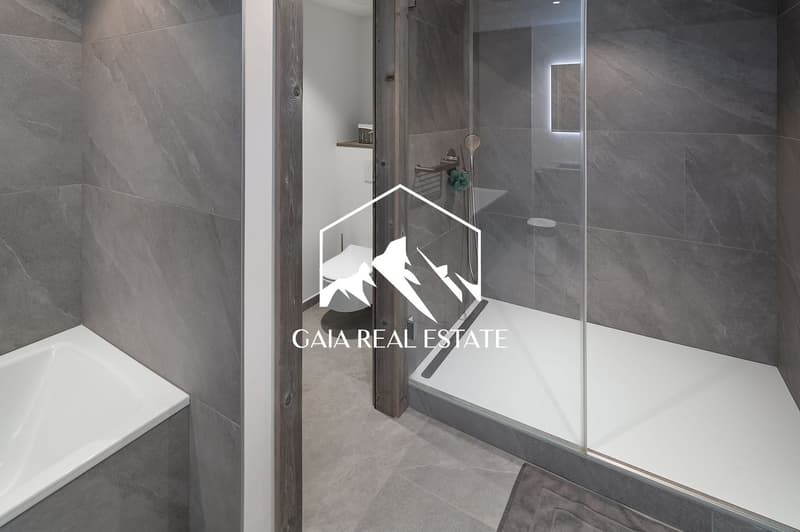 Large, modern bathroom with gray tile walls and floors, a glass shower enclosure, and a wooden accent wall.