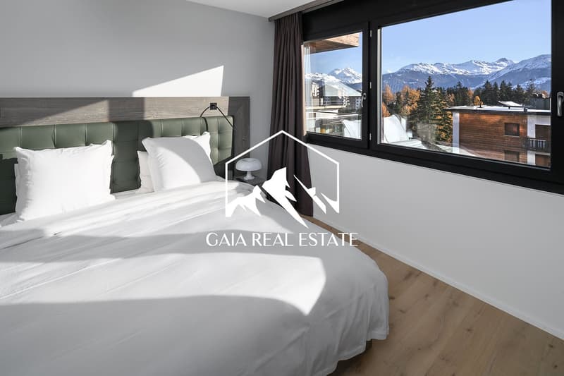 Spacious bedroom with large windows offering a scenic mountain view, grey and white color scheme, plush bedding, and modern decor