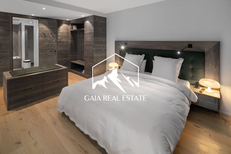 Spacious bedroom with wooden accent walls, large bed with dark headboard, bedside tables with lamps, built-in wardrobe, and hardwood flooring.