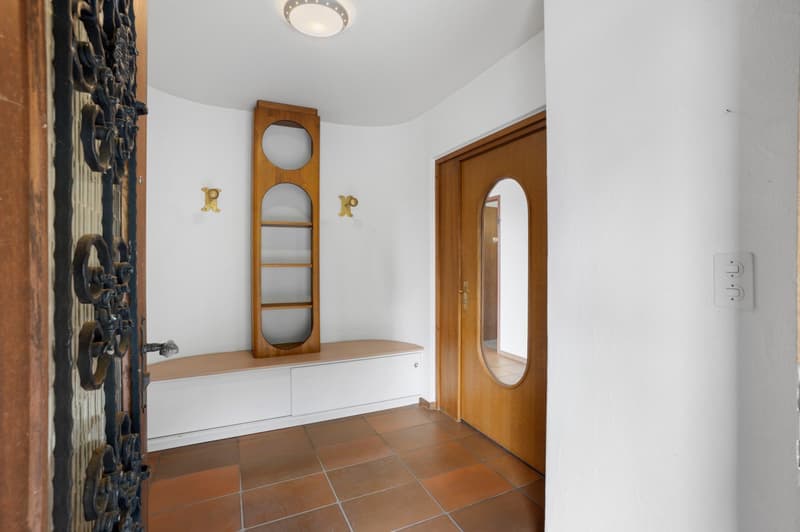 Entryway: wooden door, wooden bench, oval mirror, tiled floor, wall lamp