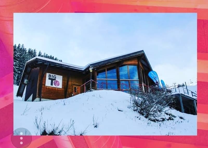 Wooden ski chalet building, big windows, covered by snow, mountain background