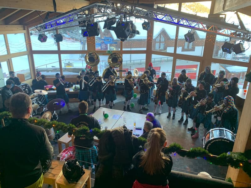 a room, a group of musicians are performing, people are watching, big windows, Christmas decorations, stage with instruments