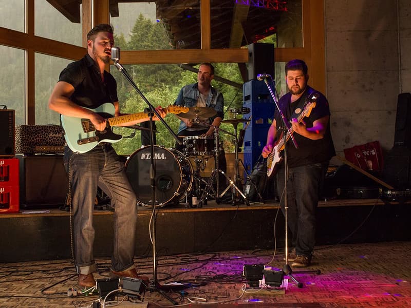 A band performing with guitar, drum set, and microphones on stage with colorful lighting.