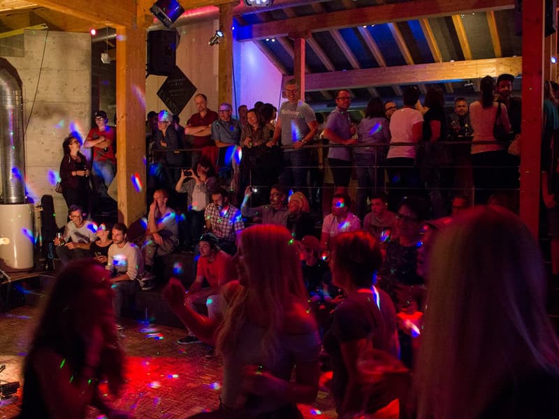 large group of people, disco lights, balcony, stage, red lights, wooden ceiling beams