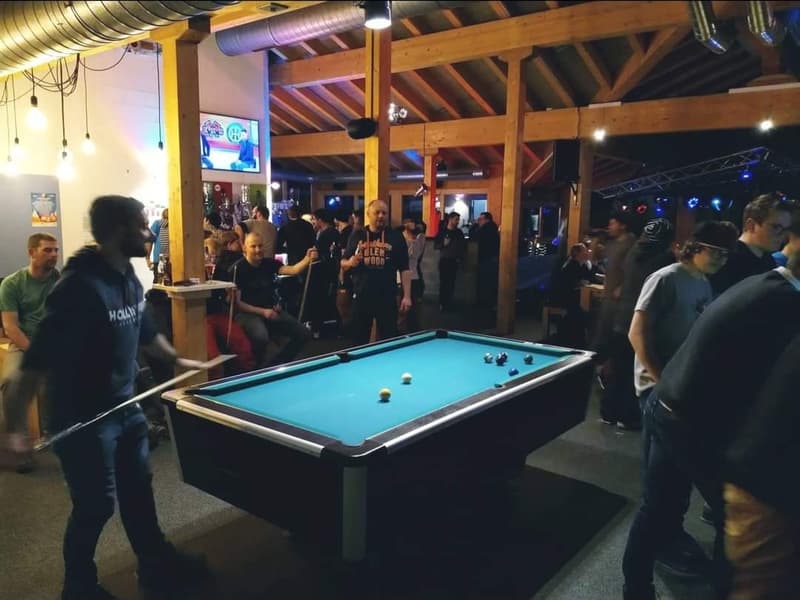 Billiard room with players and people sitting in the background, a pool table in the foreground.