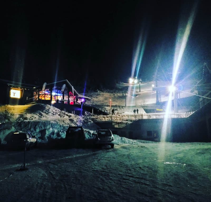Mountain ski lodge with 4 cars parked in front, night time.