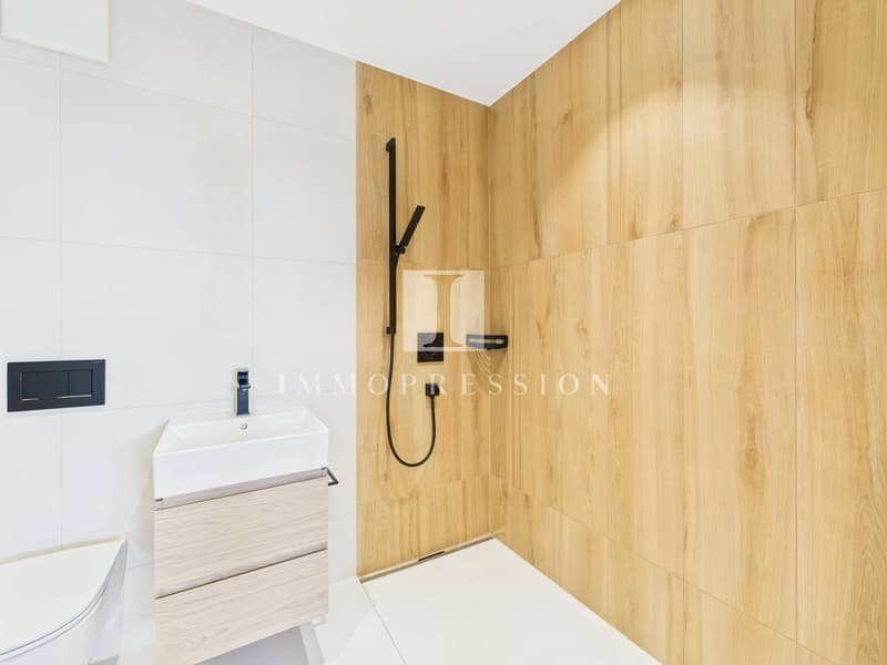 modern bathroom with white tiles, wooden wall, white sink, black shower head, white toilet