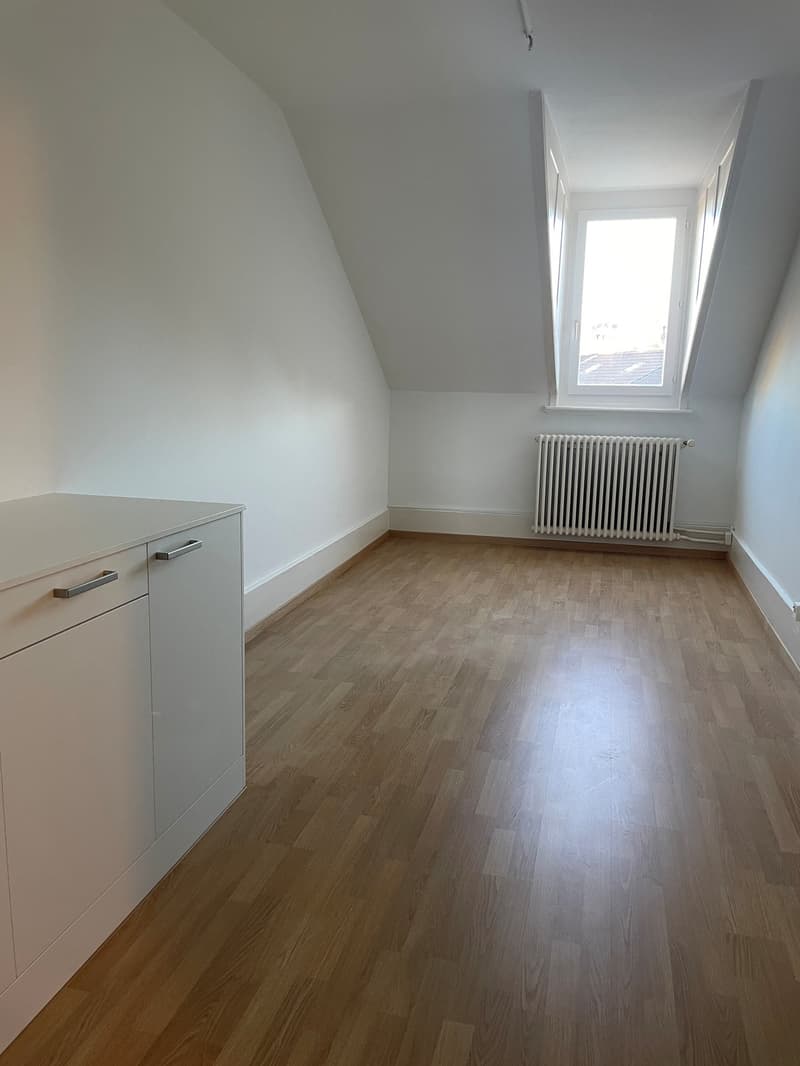 Empty room with wooden floors, white walls, a white cabinet, and a white radiator. Windows at the ceiling.