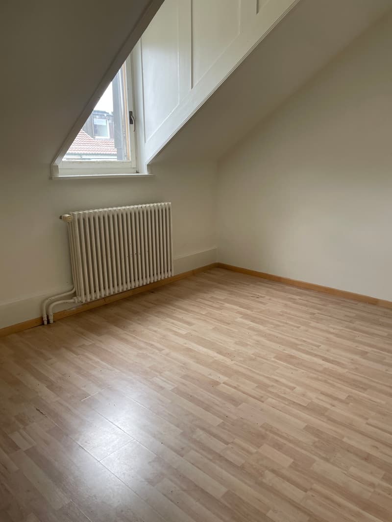 A room with wooden floor, white walls, a window, and a radiator