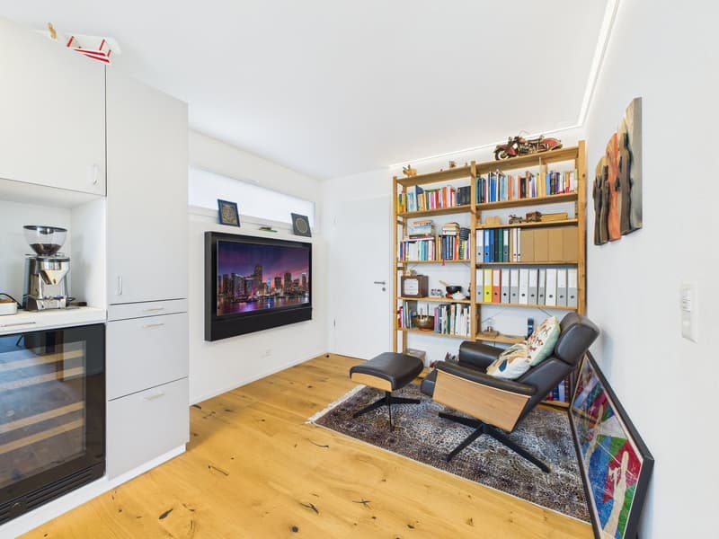 Small cozy room with armchairs, bookshelf, television, kitchen area with coffee maker and wine fridge