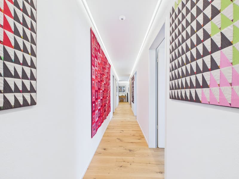 long hallway with wooden floors, white walls, colorful quilts, 2 doors at the end
