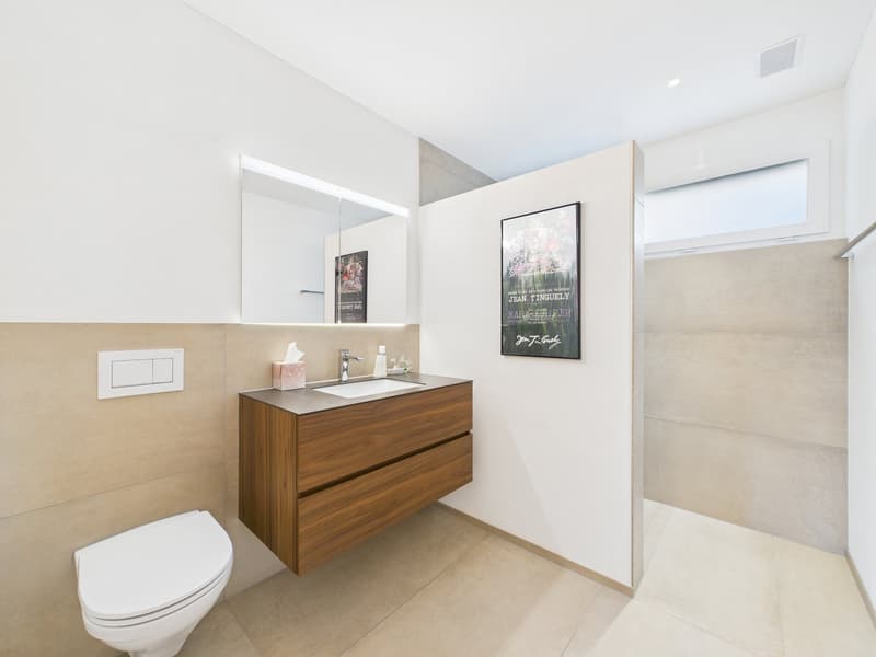 modern bathroom with a white toilet, wooden vanity with a sink, large mirror, and a shower area with tiled walls