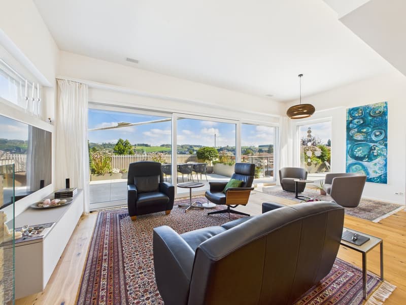 open living room with modern furnishings, large windows, leather couch, coffee table, paintings, balcony with plants and scenic view