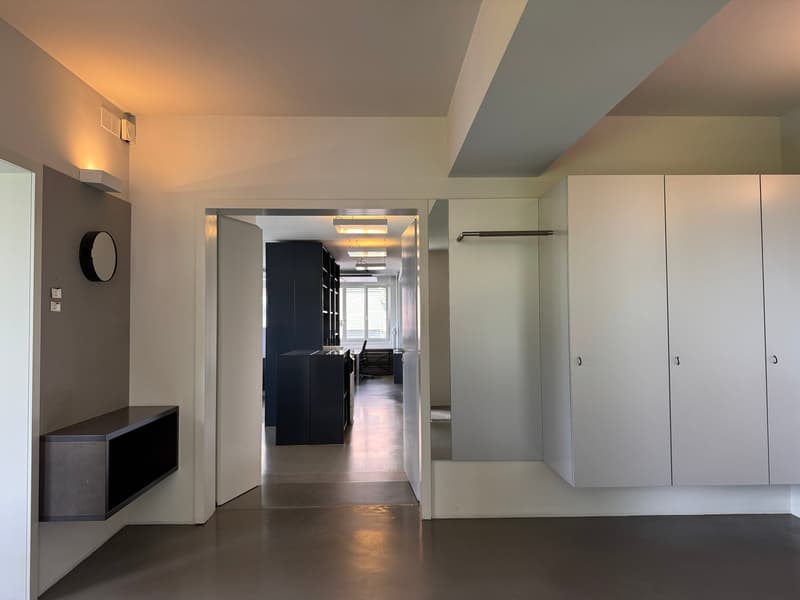 Empty room with white walls, gray floor, open door, built-in cabinets, and a mirror.