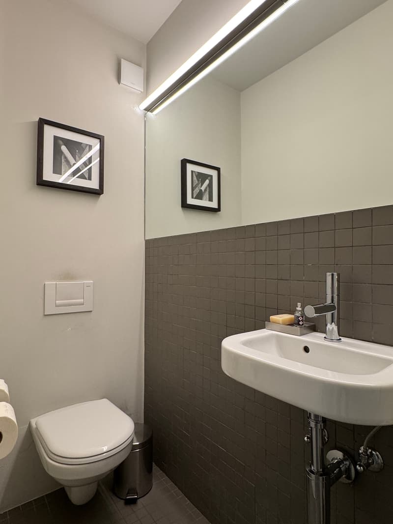 Bathroom with white toilet, sink, mirror, and tiled walls