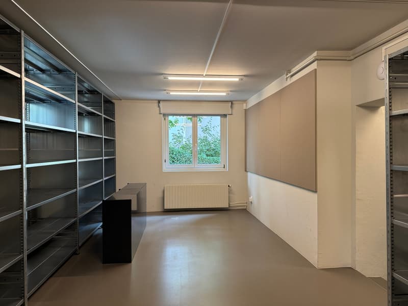 Empty room with metal shelves, a black desk, a window, and a radiator