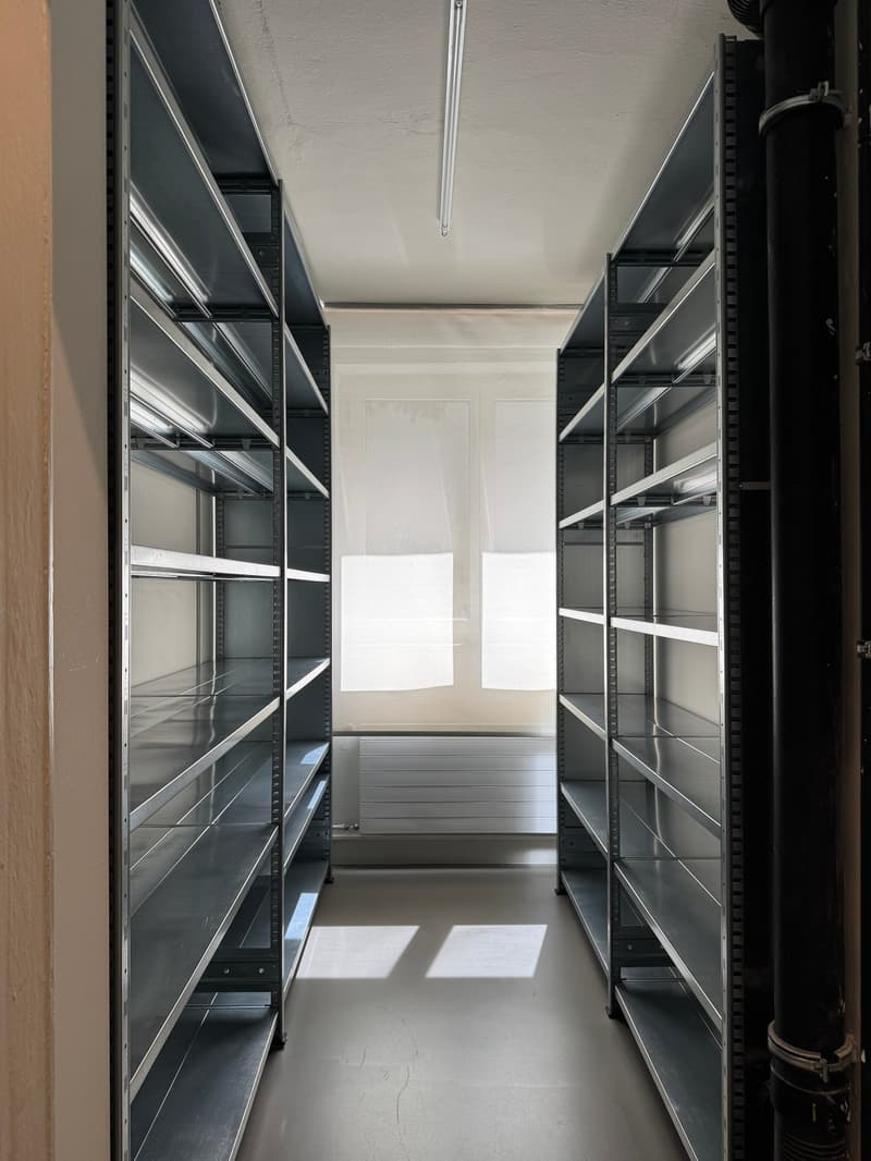 Empty room with metal shelves, white walls, white floor, windows with white curtains, metal pipe