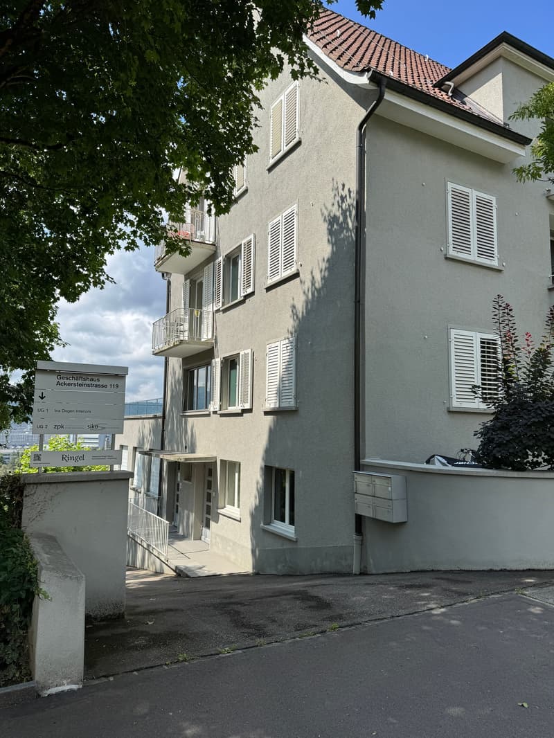 3 story building, gray exterior, white shutters, balconies, entrance with stairs