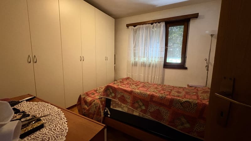 Spacious bedroom with large wardrobe, double bed with patterned bedding, and a window with curtains.