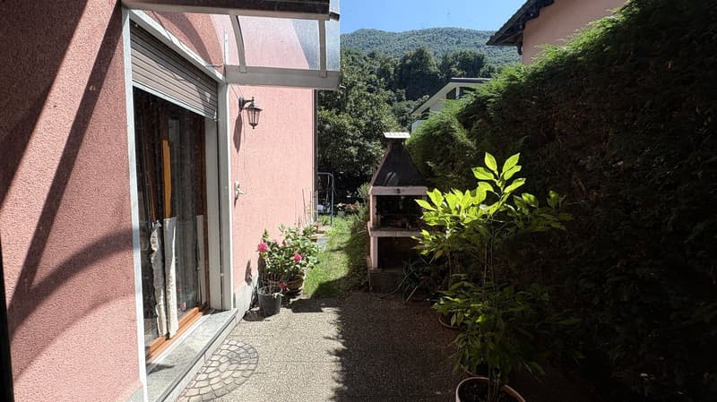 Two-story house with pink exterior, large windows, covered patio or balcony, outdoor fireplace, and lush greenery surrounding the property with a view of the mountains in the background.