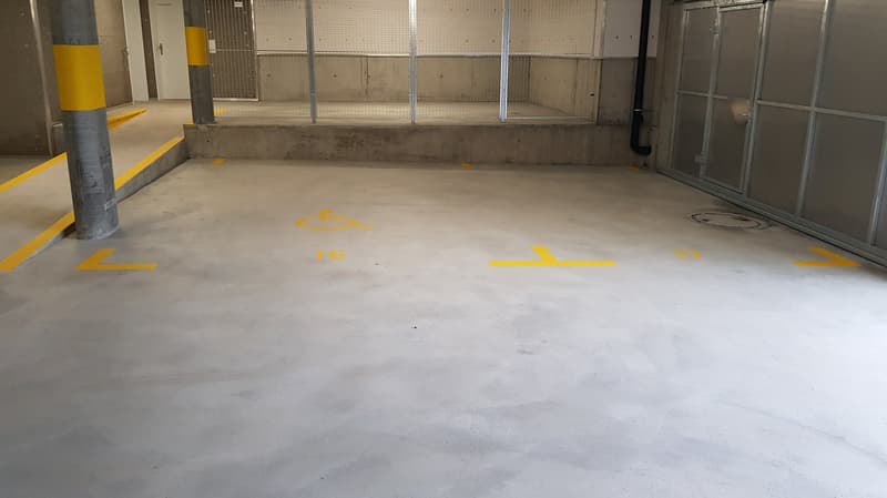 Concrete floor with yellow markings indicating parking spaces, concrete walls, and glass windows.