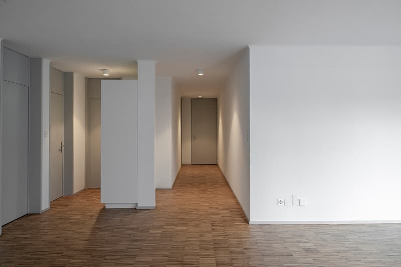 Empty hallway with wooden floor, white walls, and ceiling lights