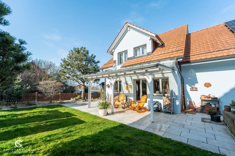 2 story house, white exterior, brown roof, covered patio, wooden chairs, solar panels