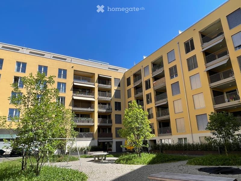 Multi-story apartment building with yellow exterior, balconies, and trees in the courtyard area