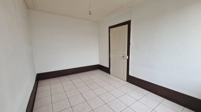 Empty room with white walls, white floor, and one door. White ceiling with hanging light.