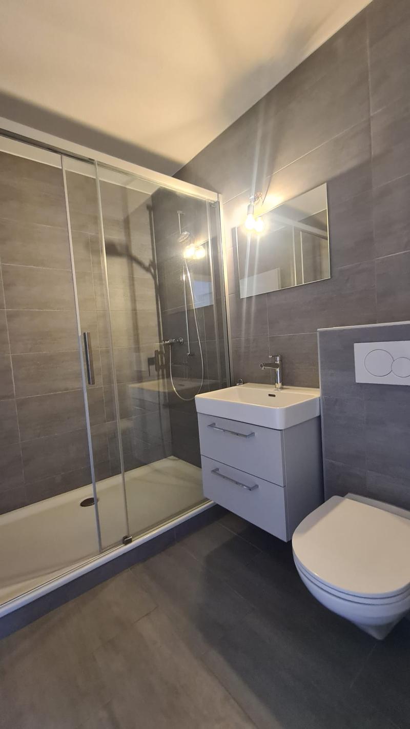 modern bathroom with shower, sink, toilet, mirror, and gray tiles