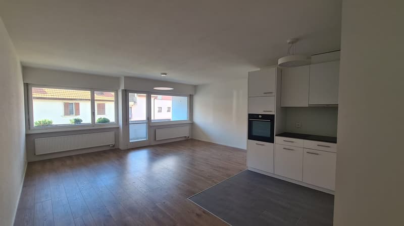 empty room, wooden floor, white walls, kitchen area with oven, windows, radiators