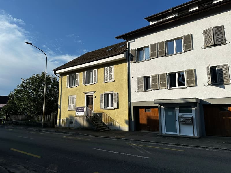2-story yellow house with white shutters, wooden stairs, metal railing, attached garage, white exterior adjacent building with windows and shutters