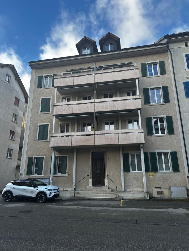 Multi-story building with balconies, concrete walls, stairs to the entrance, glass windows with shutters