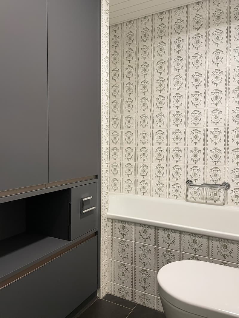 Bathroom with grey cabinets, patterned tiles, bathtub, and toilet
