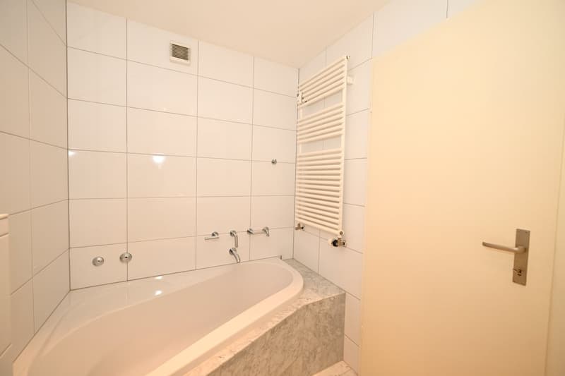 Bathroom with white tiles, bathtub, and towel rack